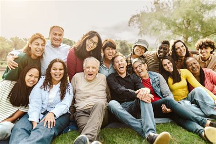 a group of people sitting next to each other on top of a grass covered field