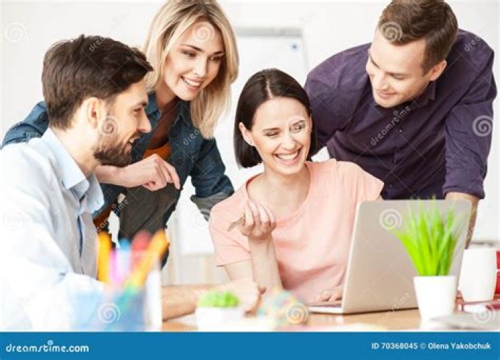 Four colleagues are working together around a laptop, smiling. One of the colleagues is pointing at the screen. 