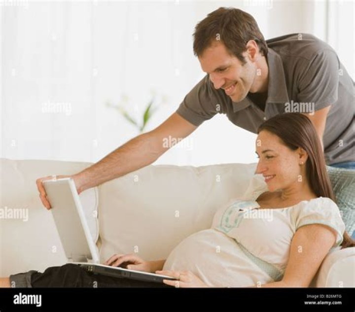 Pregnant Hispanic couple looking at laptop Stock Photo Alamy