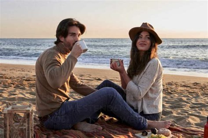 two young people sitting at a table with a laptop and coffee in front